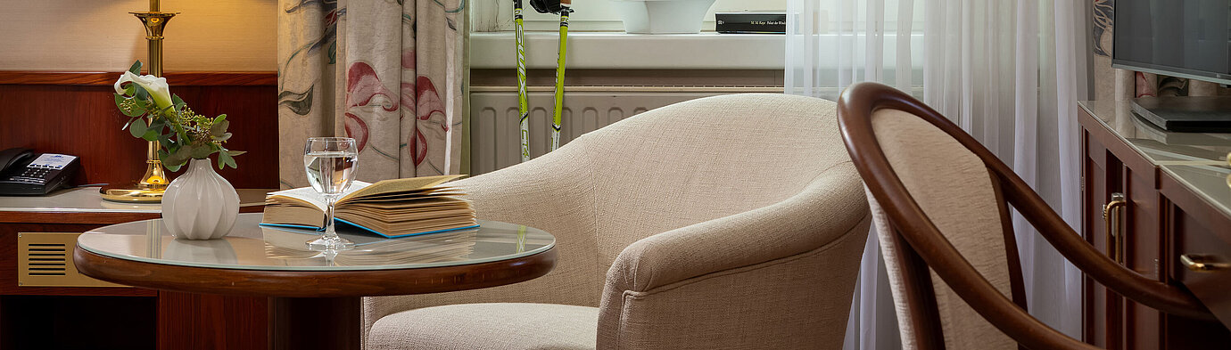 Seating area in the classic single room with armchair, table, lamp and window view at Maritim Hotel Bad Wildungen.