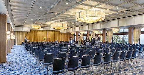 Saal Maritim in the Maritim Hotel Kiel, large conference room with row seating, chandeliers and stage, staff prepare the room.