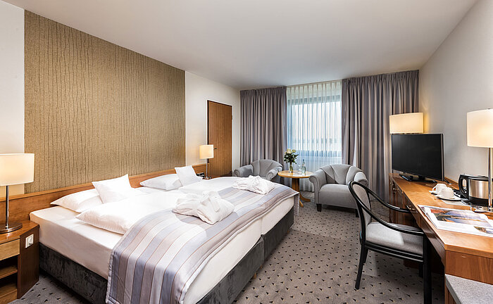 Superior double room with king-size bed, bathrobes, seating area, and desk at Maritim Hotel Hannover.