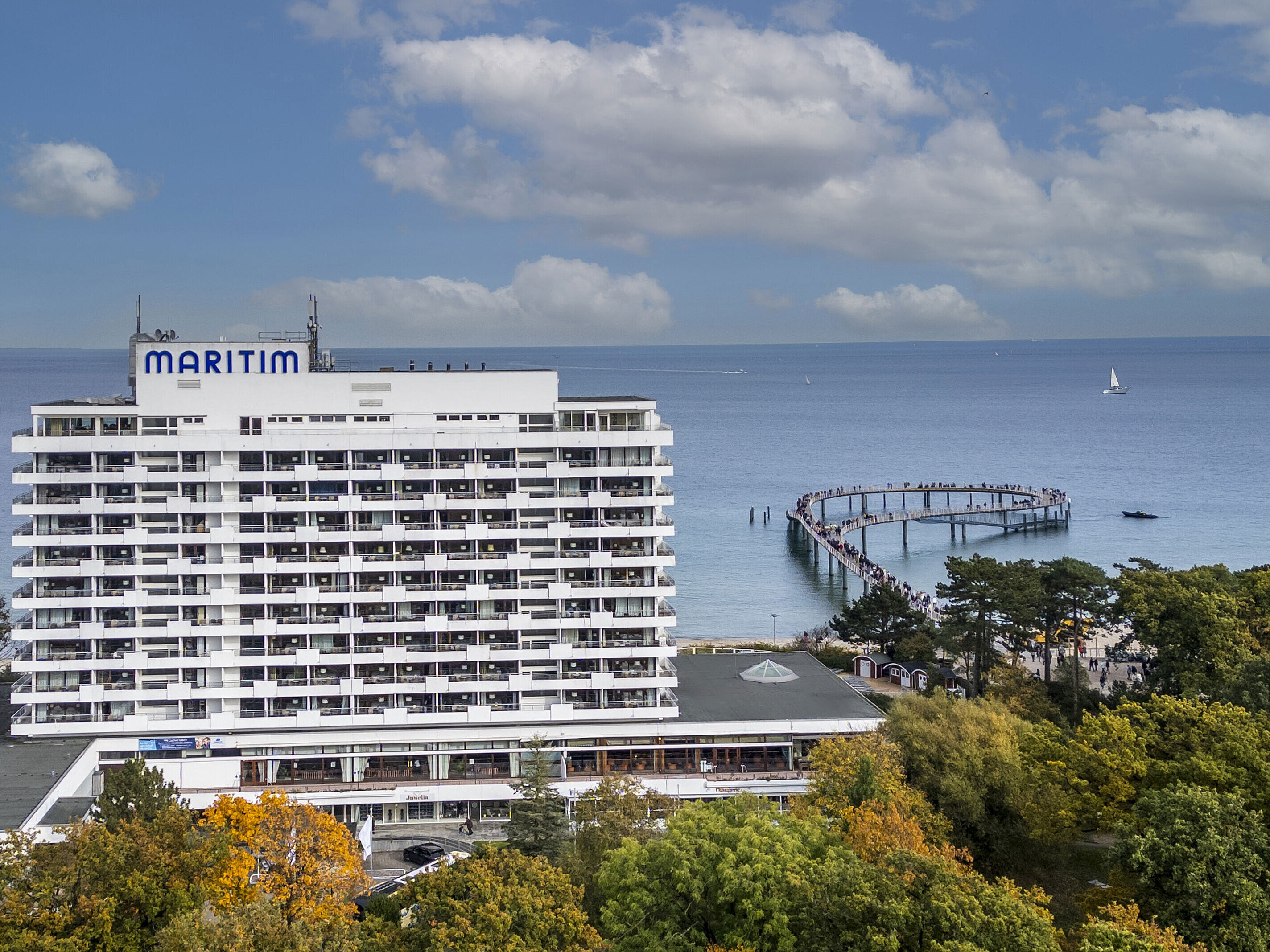 Maritim Seehotel Timmendorfer Strand overlooking the pier and Baltic Sea, surrounded by trees and a blue sky.