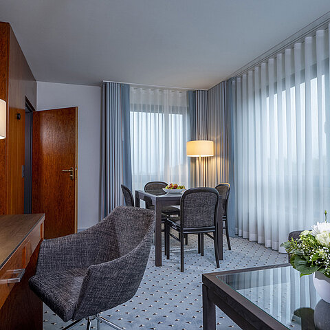 Elegant suite living room at Maritim Hotel Bremen with cozy seating area, desk, TV, and fresh flowers for decoration.