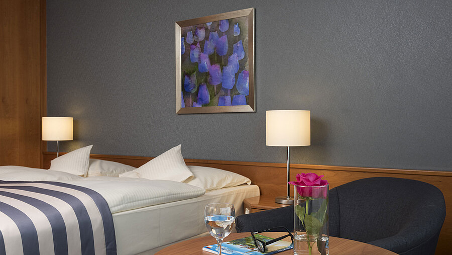 Detail at Maritim Hotel Ulm: table with rose, water, glasses and travel brochure near bed
