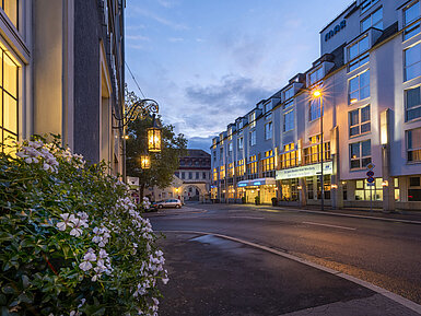 Evening exterior view of the Maritim Hotel Würzburg with illuminated facade and historic gateway in the background