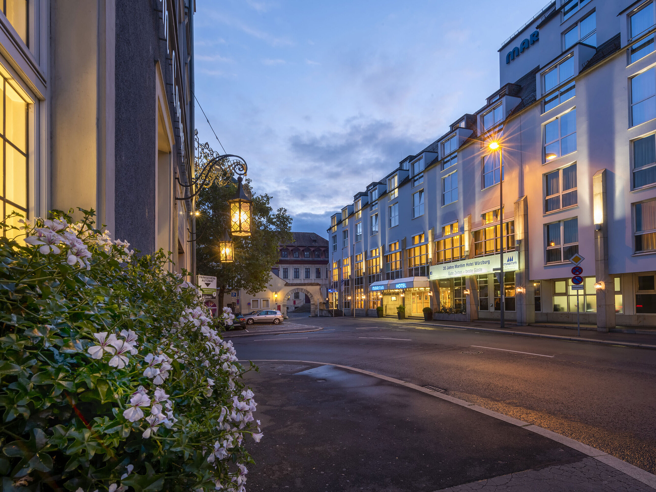Evening exterior view of the Maritim Hotel Würzburg with illuminated facade and historic gateway in the background