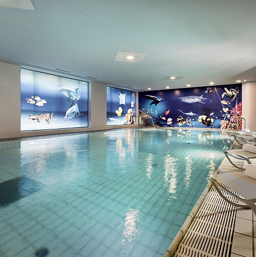 Indoor pool at the Maritim proArte Hotel Berlin with relaxing loungers and stunning underwater-themed wall decor.