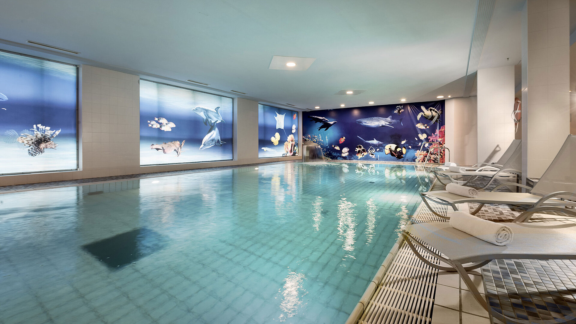Indoor pool at the Maritim proArte Hotel Berlin with relaxing loungers and stunning underwater-themed wall decor.
