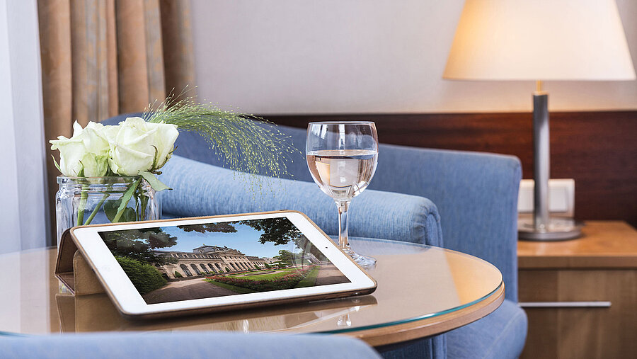 Cozy seating area at Maritim Hotel Fulda with tablet, glass of water, and white roses on a glass table.