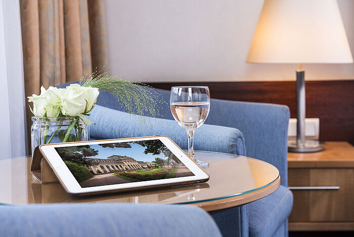 Cozy seating area at Maritim Hotel Fulda with tablet, glass of water, and white roses on a glass table.
