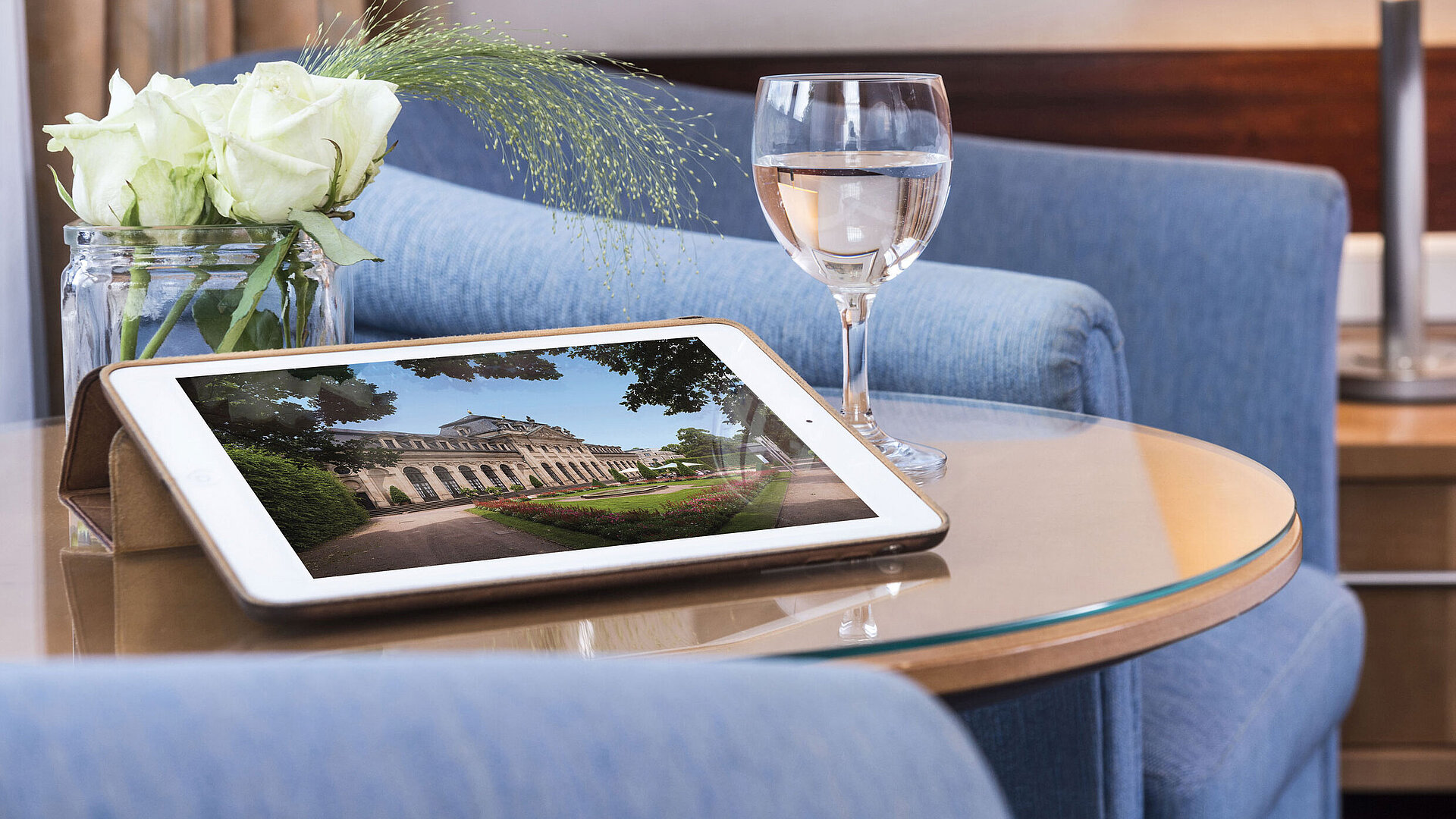 Cozy seating area at Maritim Hotel Fulda with tablet, glass of water, and white roses on a glass table.