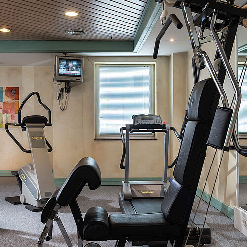 Gym at Maritim Hotel Magdeburg with modern equipment like a treadmill, exercise bike, and strength station for effective workouts.
