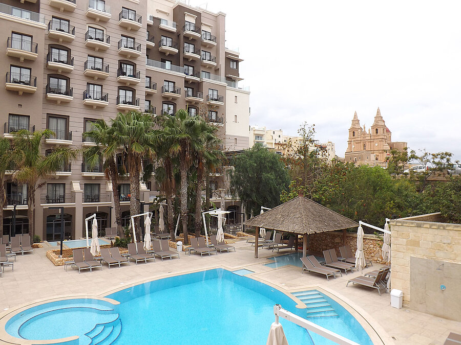 Large outdoor pool with sun loungers, palm trees and views of the hotel and surrounding city