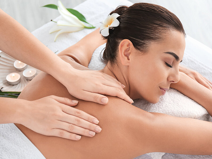 Woman relaxing during soothing back massage in spa with flower in hair