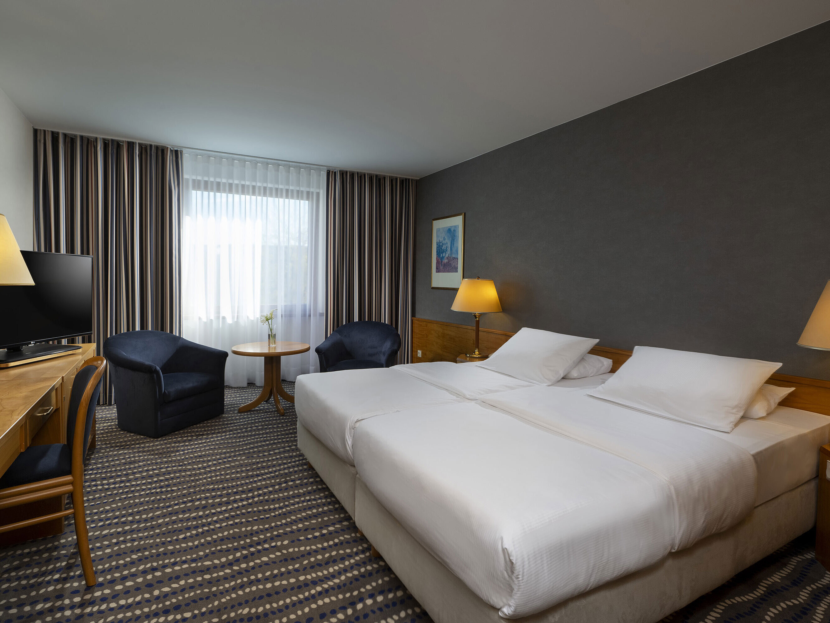 Hotel room with double bed, TV, desk, and cozy seating area, ideal for relaxation and comfort