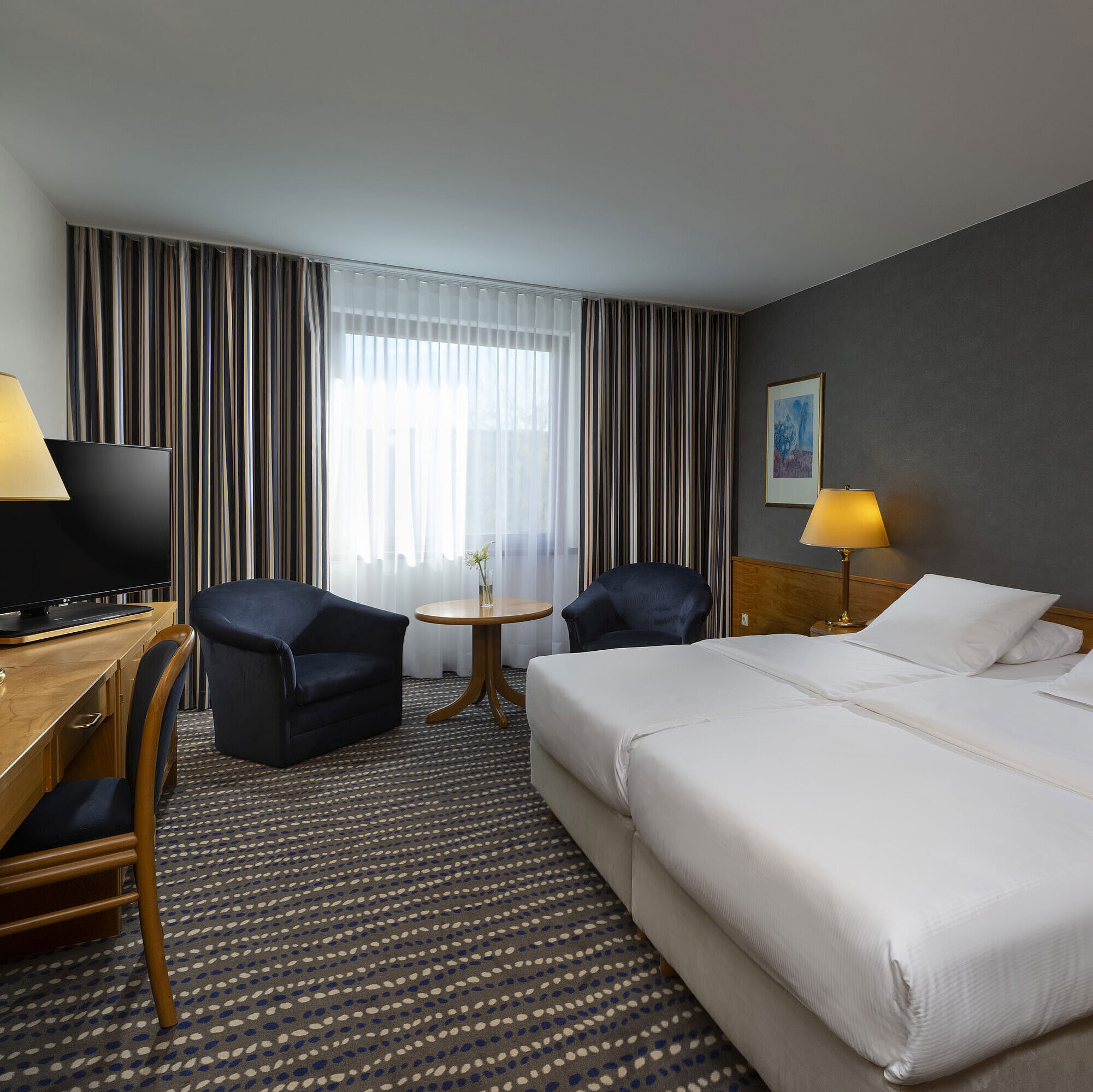Hotel room with double bed, TV, desk, and cozy seating area, ideal for relaxation and comfort
