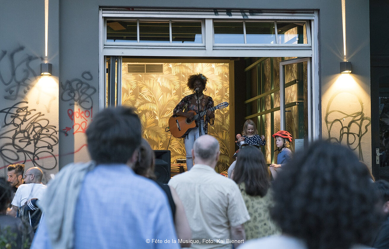 Street concert during Fête de la Musique with singer performing for an audience outside in a summer evening atmosphere
