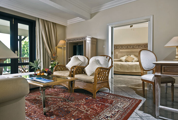 Stylish suite living area with seating, wooden furniture, rug and view into the bedroom