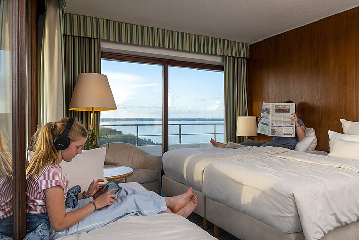 Family room with park view at Maritim Hotel Timmendorfer Strand, a child with tablet and a person reading a newspaper, with sea view.