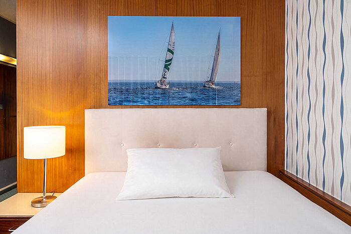 Queen-size bed in the Classic Queen Room with bedside lamp and maritime wall art