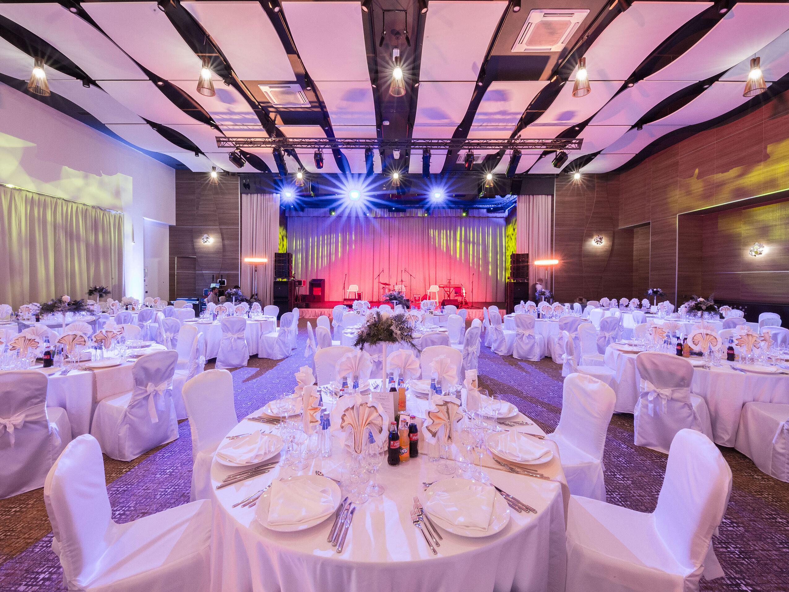 Elegant banquet hall with round tables, stage and colourful event lighting