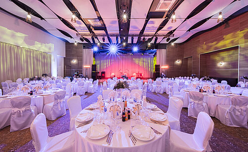 Elegant banquet hall with round tables, stage and colourful event lighting