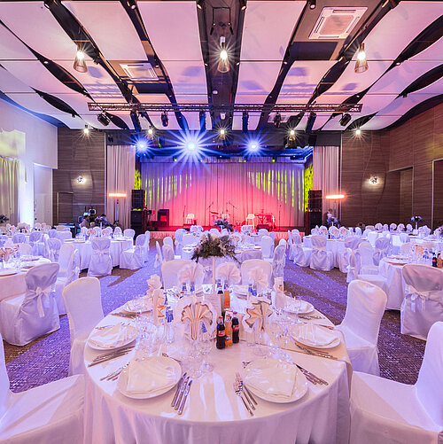 Elegant banquet hall with round tables, stage and colourful event lighting