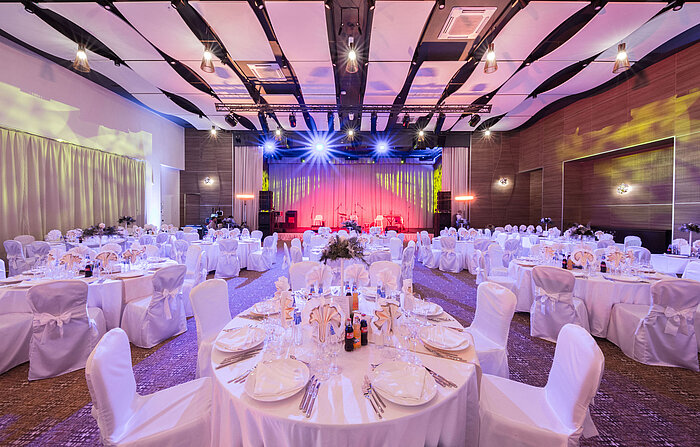 Elegant banquet hall with round tables, stage and colourful event lighting