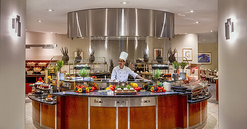 Chef at the show cooking station at Maritim proArte Hotel Berlin, surrounded by fresh vegetables and herbs.