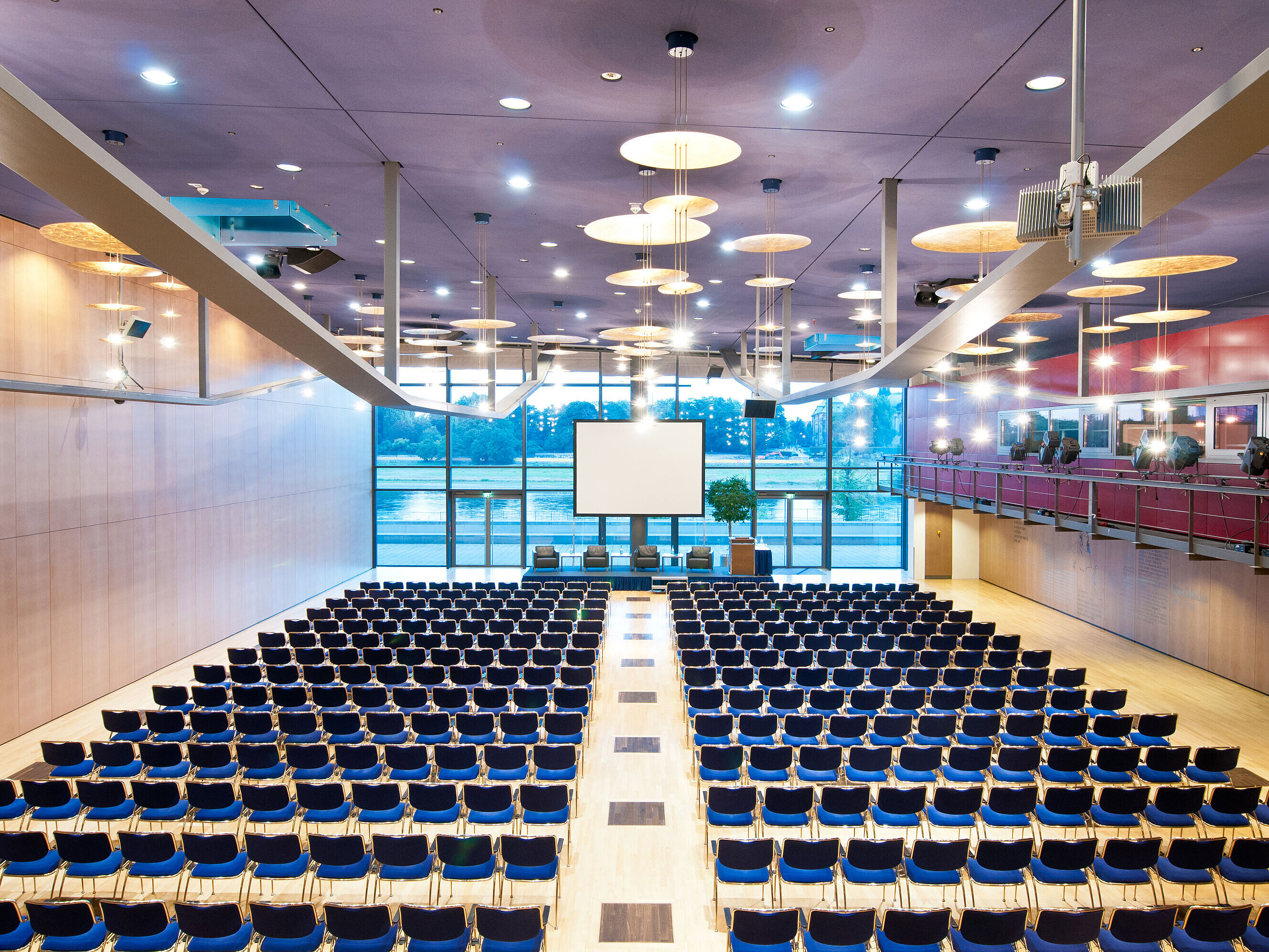 Large conference hall in Maritim Hotel Dresden with rows of blue chairs and a view of the Elbe River.