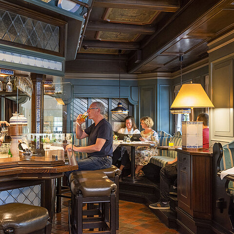 Cozy hotel bar in traditional style with guests enjoying drinks and a bartender pouring beer.