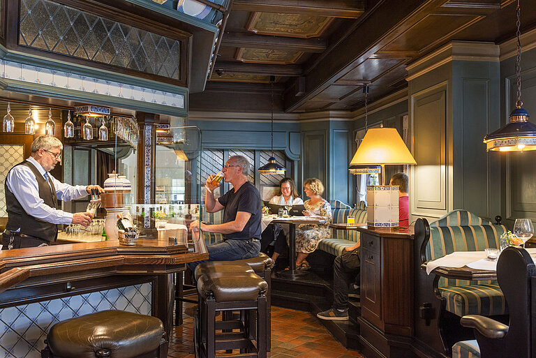 Cozy hotel bar in traditional style with guests enjoying drinks and a bartender pouring beer.