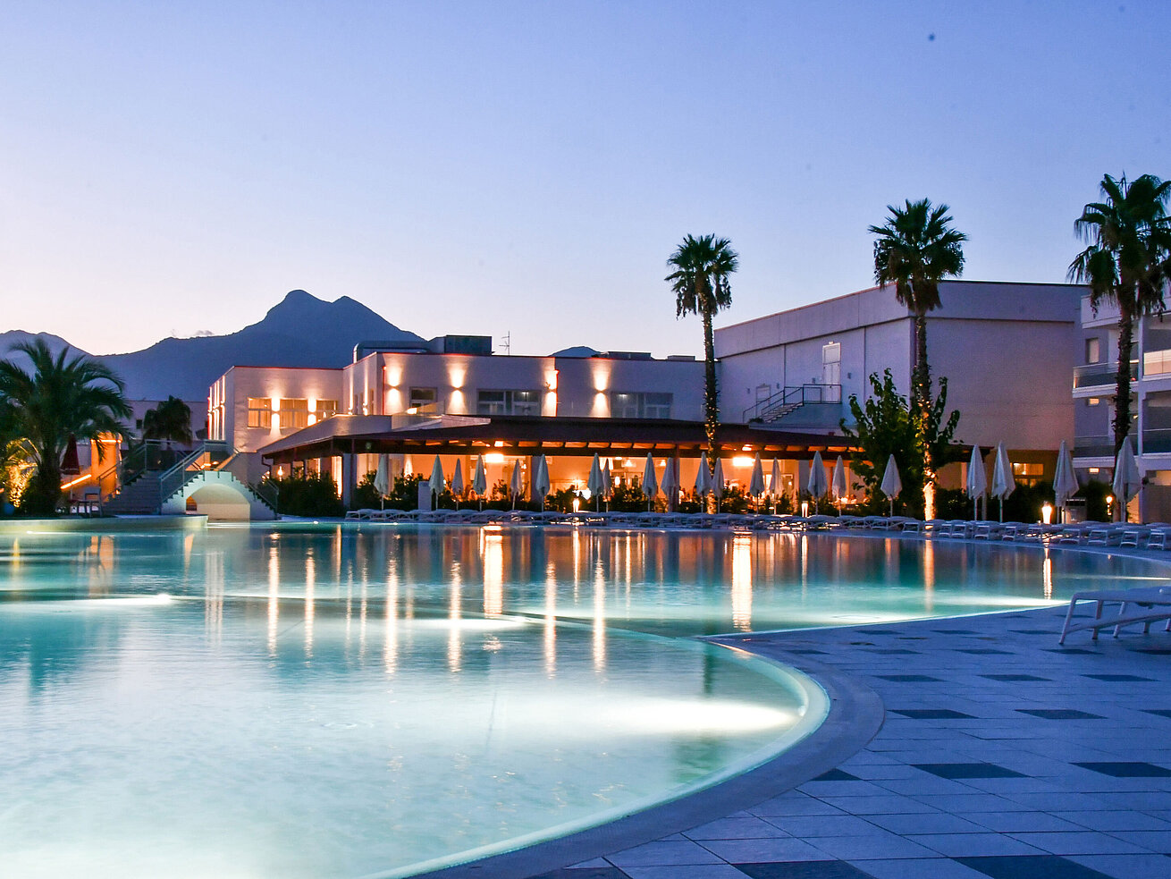 Evening lights at the pool of Maritim Resort Calabria with palm trees and mountain backdrop