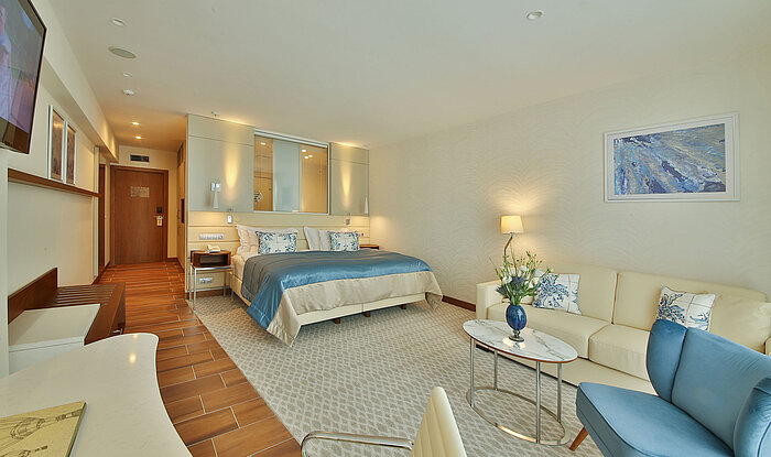 Spacious hotel room with double bed, seating area and modern interior in warm colours
