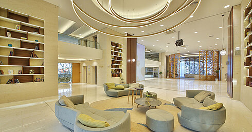 Large hotel lobby with modern ring lighting, lounge seating and decorative shelves