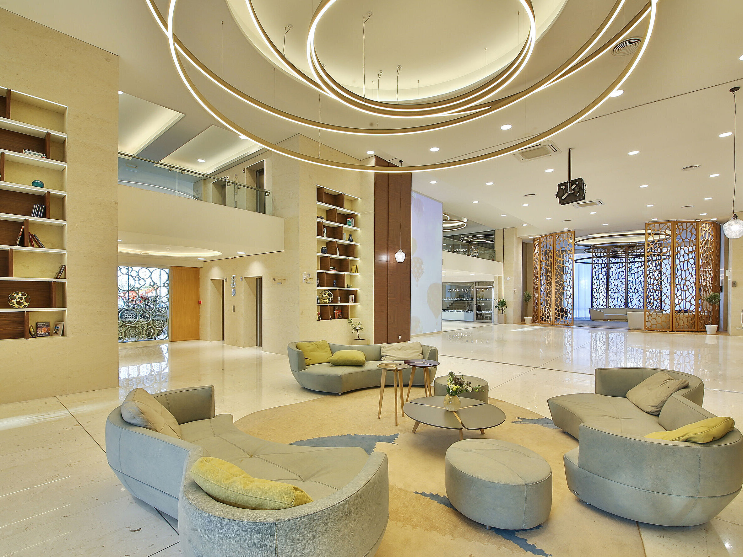 Large hotel lobby with modern ring lighting, lounge seating and decorative shelves