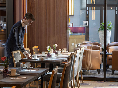 Staff member sets a table in the Classico restaurant of Maritim Hotel Düsseldorf, surrounded by elegant decor.