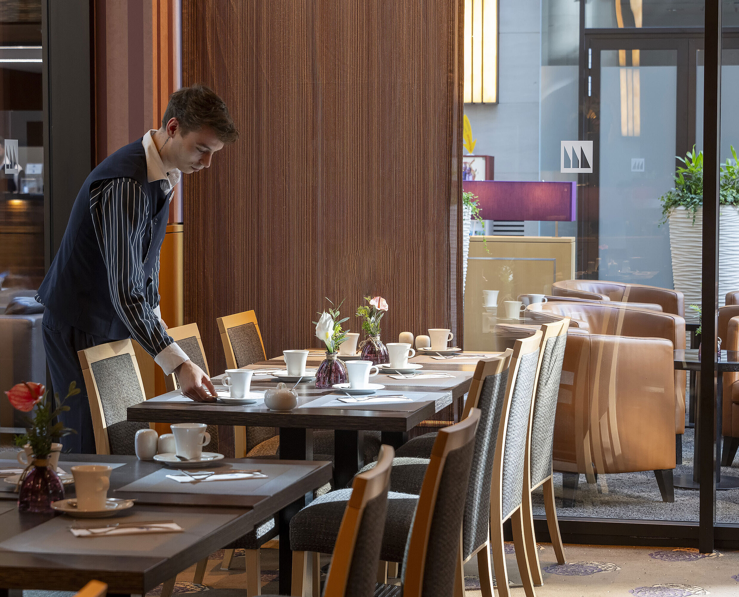 Staff member sets a table in the Classico restaurant of Maritim Hotel Düsseldorf, surrounded by elegant decor.