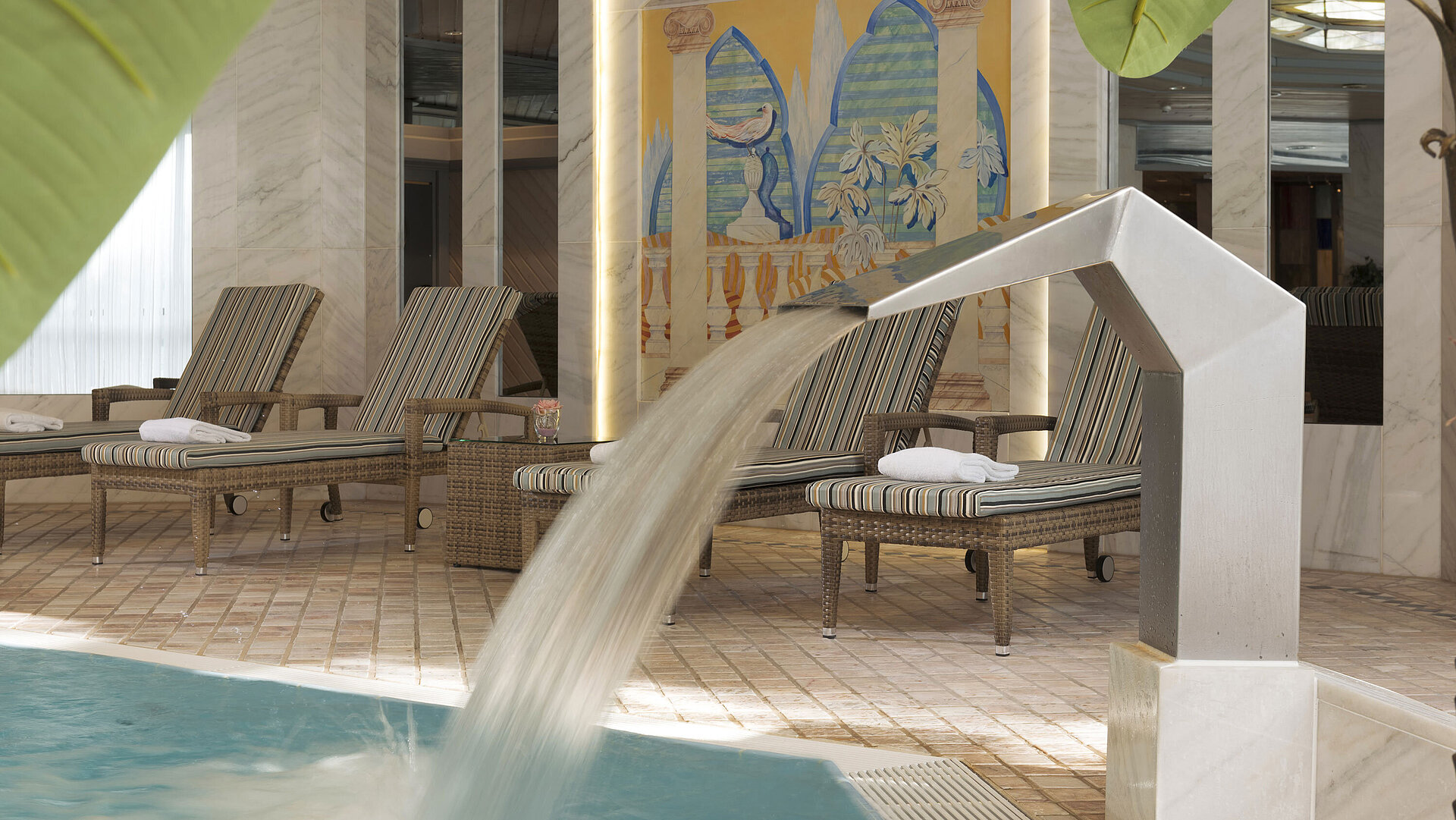 Modern indoor pool with waterfall and loungers at Maritim Hotel Ulm for your relaxing getaway.