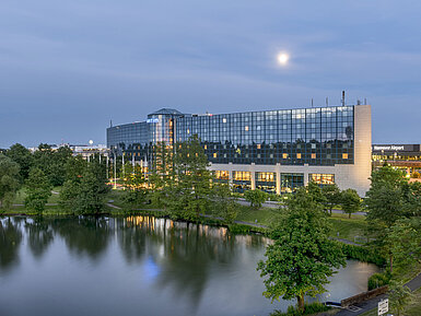 Illuminated Maritim Hotel Hannover with a glass facade and lake reflection at dusk.