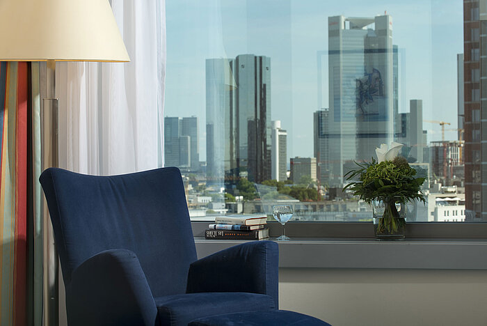 View from a suite at Maritim Hotel Frankfurt with skyline view, blue armchair, and decorative flower arrangement.