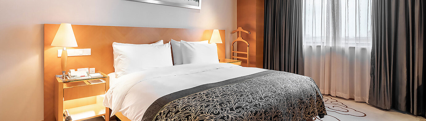 現代化酒店客房配備舒適雙人床、暖色燈光、大窗戶，床頭上方懸掛時尚藝術品