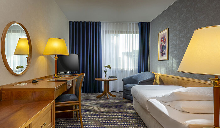 Cosy room with desk, bed and armchair at Maritim Hotel Magdeburg