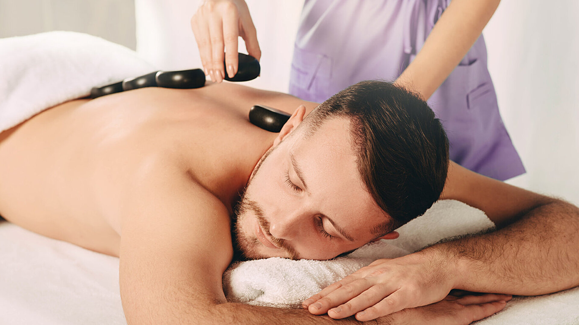 © Peakstock - AdobeStock.com Man enjoying relaxing hot stone massage in spa for deep relaxation