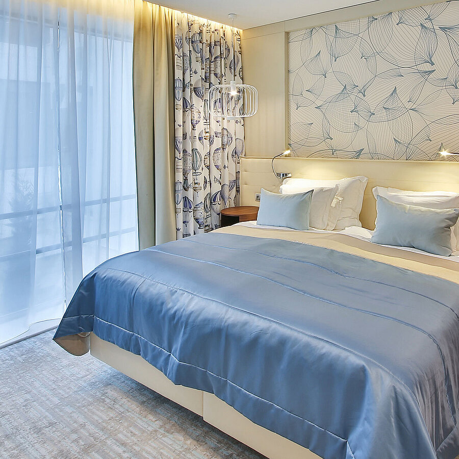 Modern hotel room with double bed, blue accents and large windows with curtains