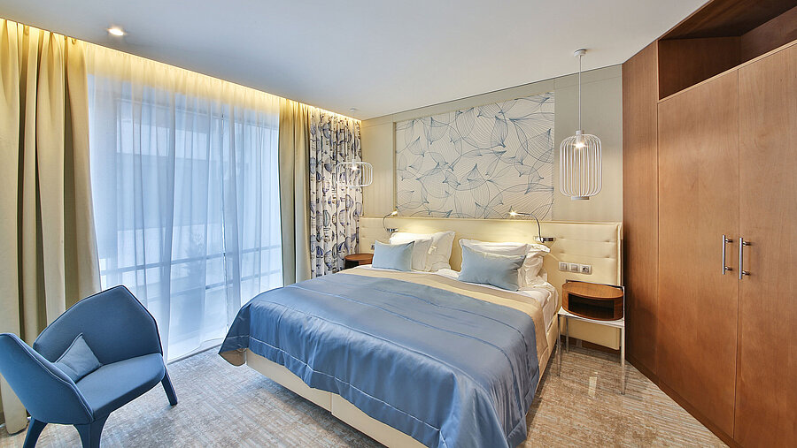 Modern hotel room with double bed, blue accents and large windows with curtains