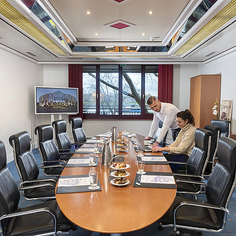 Two people working in the Salon Boardroom at Maritim Cologne with laptops at a conference table with drinks and snacks.