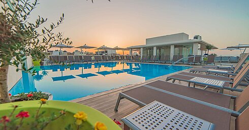 Outdoor pool with sun loungers and parasols during atmospheric sunset