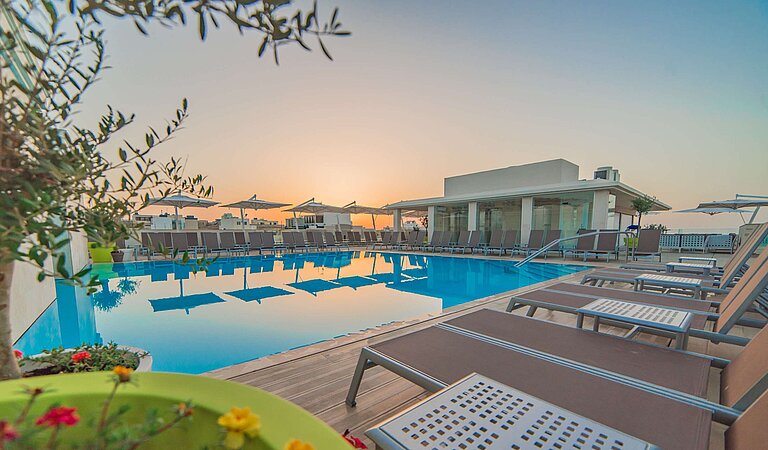 Outdoor pool with sun loungers and parasols during atmospheric sunset
