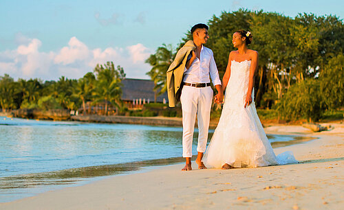 Wedding couple walking barefoot along the beach in sunlight – romantic beach wedding at Maritim Resort