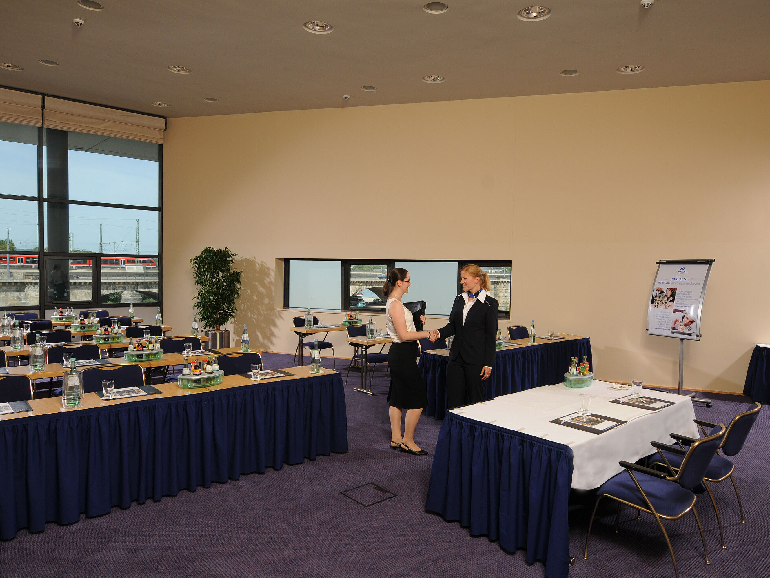 Bright meeting room in Maritim Hotel Dresden with set tables, flipchart, and two people shaking hands.