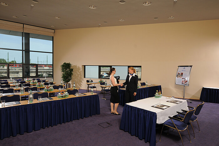 Bright meeting room in Maritim Hotel Dresden with set tables, flipchart, and two people shaking hands.